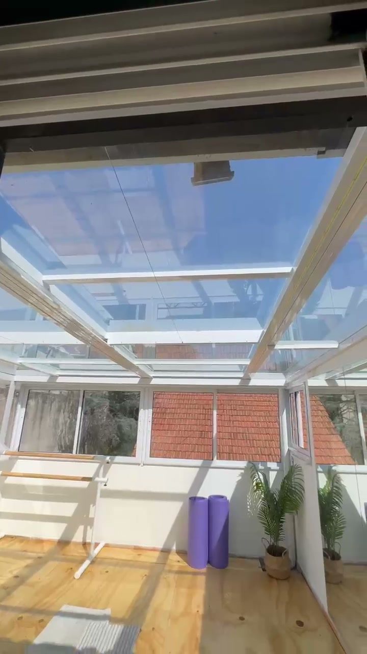Sala con techo de vidrio y estructura blanca, con lámina de control solar que deja ver el cielo